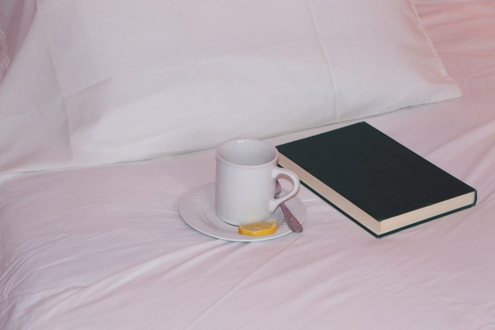 Lit garni d'un drap blanc, d'un oreiller, d'un livre et d'une tasse.
